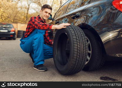 Male worker in uniform fixing problem with tire, tyre service. Vehicle repair service or business, man repairing broken wheel. Male worker in uniform fix problem with tire
