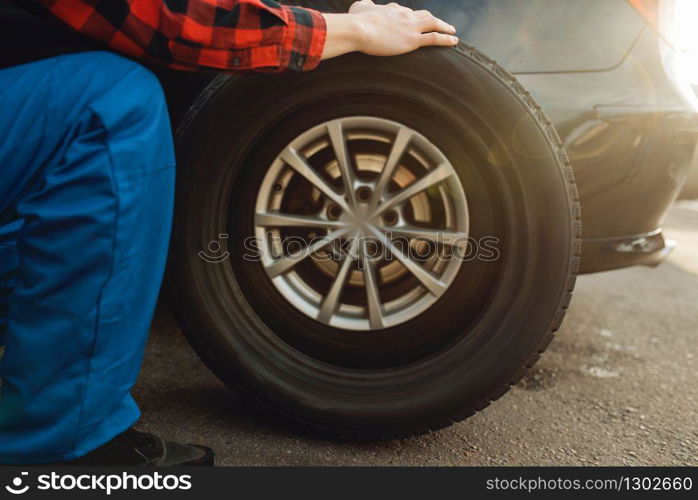 Male worker in uniform fixing problem with tire, tyre service. Vehicle repair service or business, man repairing broken wheel. Male worker in uniform fix problem with tire