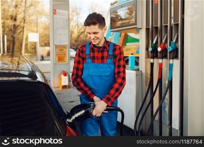 Male worker in uniform fuels car on gas station, fuel filling. Petrol fueling, gasoline or diesel refuel service. Male worker in uniform fuels car on gas station