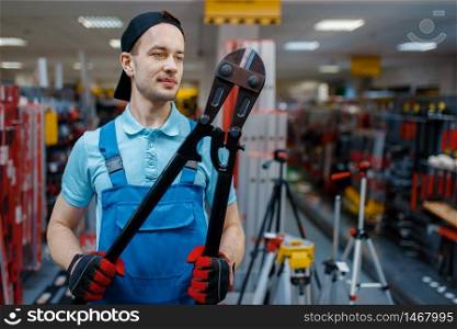 Male worker in uniform holds big metal wire cutters in tool store. Choice of professional equipment in hardware shop, instrument supermarket. Worker holds big metal wire cutters in tool store