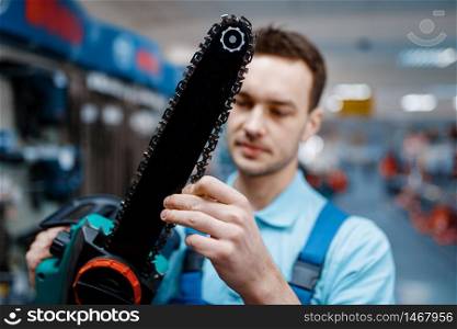 Male worker in uniform holds electric saw in tool store. Choice of professional equipment in hardware shop. Worker in uniform holds electric saw in tool store