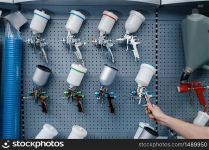 Male worker in uniform holds pneumatic paint spray gun in tool store. Choice of professional equipment in hardware shop, instrument supermarket. Male worker holds pneumatic paint gun, tool store