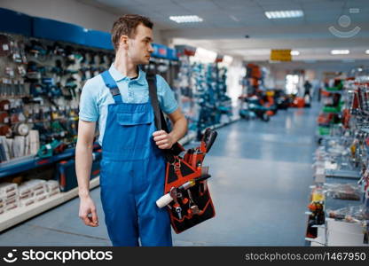 Male worker in uniform holds toolbox in tool store. Choice of professional equipment in hardware shop. Male worker in uniform holds toolbox in tool store