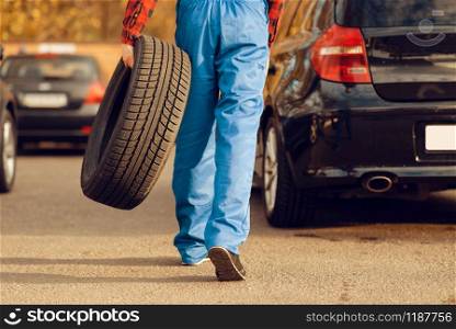 Male worker in uniform holds tyre, tire service. Vehicle repair service or business, man repairing broken wheel. Male worker in uniform holds tyre, tire service