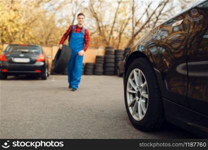 Male worker in uniform holds tyre, tire service. Vehicle repair service or business, man repairing broken wheel. Male worker in uniform holds tyre, tire service