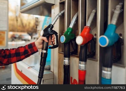 Male worker in uniform takes a gun at a gas station, fuel filling. Petrol fueling, gasoline or diesel refuel service. Male worker in uniform takes a gun at gas station