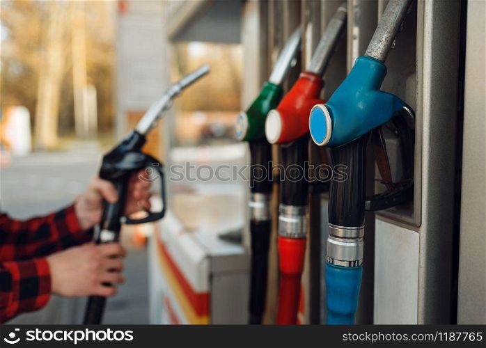 Male worker in uniform takes a gun at a gas station, fuel filling. Petrol fueling, gasoline or diesel refuel service. Male worker in uniform takes a gun at gas station