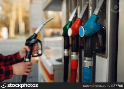 Male worker in uniform takes a gun at a gas station, fuel filling. Petrol fueling, gasoline or diesel refuel service. Male worker in uniform takes a gun at gas station