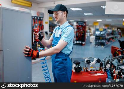 Male worker in uniform testing pneumatic nailer in tool store. Choice of professional equipment in hardware shop, instrument supermarket. Male worker testing pneumatic nailer in tool store