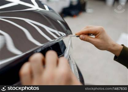 Male worker installs transparent protection film on car hood. Installation of coating that protects the paint of automobile from scratches. New vehicle in garage. Worker installs protection film on car hood