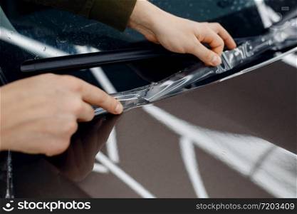 Male worker installs transparent protection film on car hood. Installation of coating that protects the paint of automobile from scratches. New vehicle in garage. Worker installs protection film on car hood