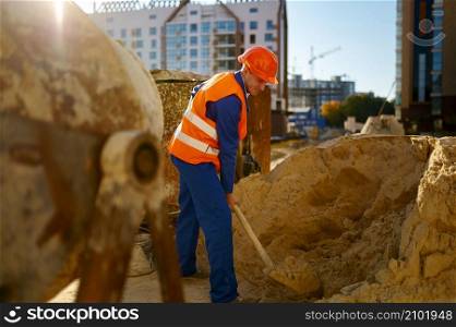 Male worker making concrete at construction site. Builder using shovel loading mixer with sand. Male worker making concrete at construction site