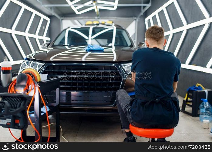 Male worker polishes car surface using polishing machine, detailing. Preparationa before installation of coating that protects the paint of automobile from scratches. Vehicle in garage, auto tuning. Male worker polishes car surface, detailing