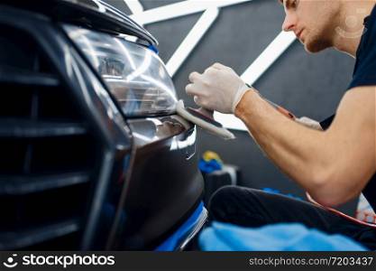 Male worker polishes front bumper using polishing machine, car detailing closeup. Preparationa before installation of coating that protects the paint of automobile from scratches, auto tuning. Male worker polishes front bumper, car detailing