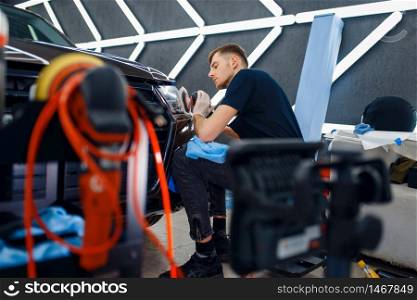 Male worker polishes headlights using polishing machine, car detailing. Preparationa before installation of coating that protects the paint of automobile from scratches. Auto tuning in workshop. Male worker polishes headlights, car detailing
