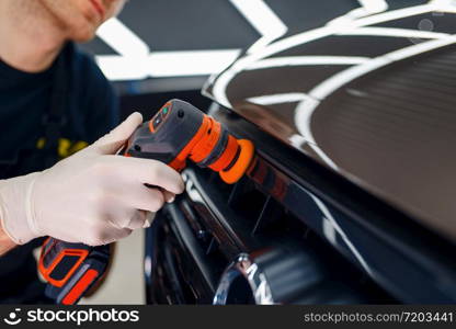 Male worker polishes radiator grille using polishing machine, car detailing closeup. Preparationa before installation of coating that protects the paint of automobile from scratches, auto tuning. Worker polishes radiator grille, car detailing