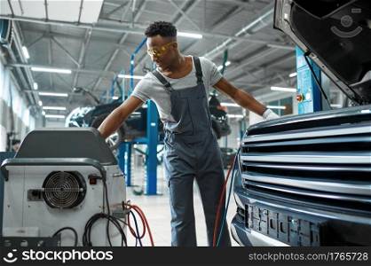 Male worker refills the air conditioner, car service. Vehicle repairing garage, man in uniform, automobile station interior on background. Male worker refills air conditioner, car service