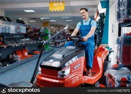 Male worker sitting on lawn mower in tool store. Choice of professional equipment in hardware shop, electrical and gas instrument supermarket. Male worker sitting on lawn mower in tool store