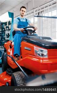 Male worker sitting on lawn mower in tool store. Choice of professional equipment in hardware shop, electrical and gas instrument supermarket. Male worker sitting on lawn mower in tool store