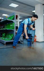 Male worker testing big electric perforator on tool store floor, humor or joke. Choice of professional equipment in hardware shop, electrical instrument supermarket. Worker testing big electric perforator, tool store