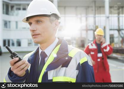 Male worker using walkie-talkie with colleague in background at shipping yard