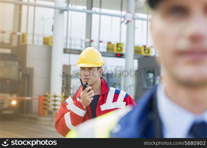 Male worker using walkie-talkie with colleague in foreground at shipyard