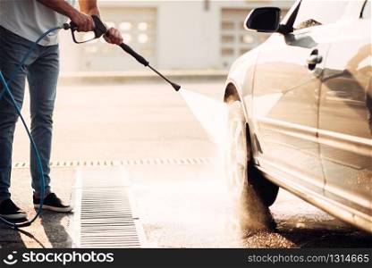 Male worker wash the car with high pressure washer. Car-wash station. Male worker wash the car with high pressure washer