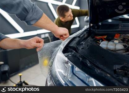 Male worker wets car fender surface with spray before applying of protection film. Installation of coating that protects the paint of automobile from scratches. New vehicle in garage, detailing. Male worker wets car fender surface, detailing