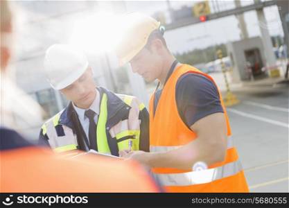 Male workers discussing over clipboard in shipping yard