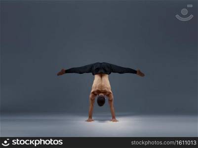 Male yoga does split on hands, back view, grey background. Strong man doing yogi exercise, asana training, top concentration, healthy lifestyle. Male yoga does split on hands, back view