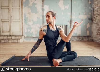 Male yoga doing flexibility exercise on mat in gym with grunge interior. Fit workout indoors, yogi studio. Male yoga doing flexibility exercise