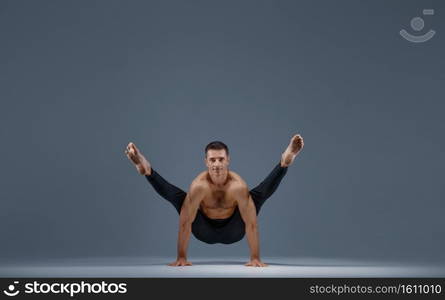 Male yoga doing stretching exercise in studio, grey background. Strong man practicing yogi , asana training, top concentration, healthy lifestyle. Male yoga doing stretching exercise in studio