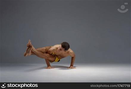 Male yoga in a difficult pose on hands, meditation, grey background. Strong man doing yogi exercise, asana training, top concentration, healthy lifestyle. Male yoga in a difficult pose on hands, meditation