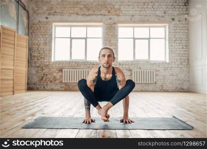 Male yoga in class, balance training. Exercise on mat in gym with grunge interior. Fit workout indoors. Male yoga in class, balance training