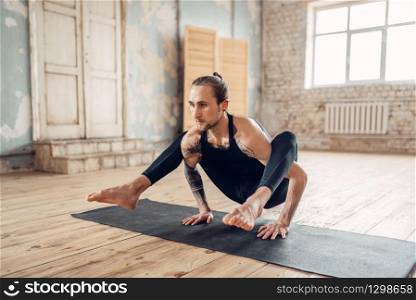 Male yoga in class, balance training. Exercise on mat in gym with grunge interior. Fit workout indoors