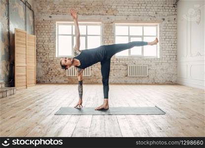 Male yoga in class, balance training. Exercise on mat in gym with grunge interior. Fit workout indoors. Male yoga in class, balance training