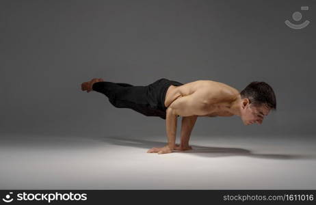 Male yoga keeps horizontal balanc on hands, meditation position, grey background. Strong man doing yogi exercise, asana training, top concentration, healthy lifestyle. Male yoga keeps horizontal balanc on hands
