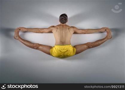 Male yoga sits on a twine, top view, grey background. Strong man doing yogi exercise, asana training, top concentration, healthy lifestyle. Male yoga sits on a twine, top view