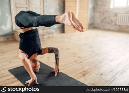 Male yoga stands on the head in gym, balance exercise on mat. Fitness workout indoors. Healthy lifestyle, meditation. Male yoga stands on the head in gym