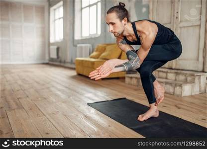 Male yoga with tattoo on hand doing balance exercise on mat in gym with grunge interior. Fit workout indoors. Male yoga doing balance exercise on mat in gym