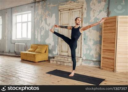 Male yoga with tattoo on hand doing balance exercise on mat in gym with grunge interior. Fit workout indoors. Male yoga doing balance exercise on mat in gym