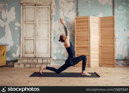Male yoga with tattoo on hand doing exercise in gym with grunge interior. Fitness training indoors