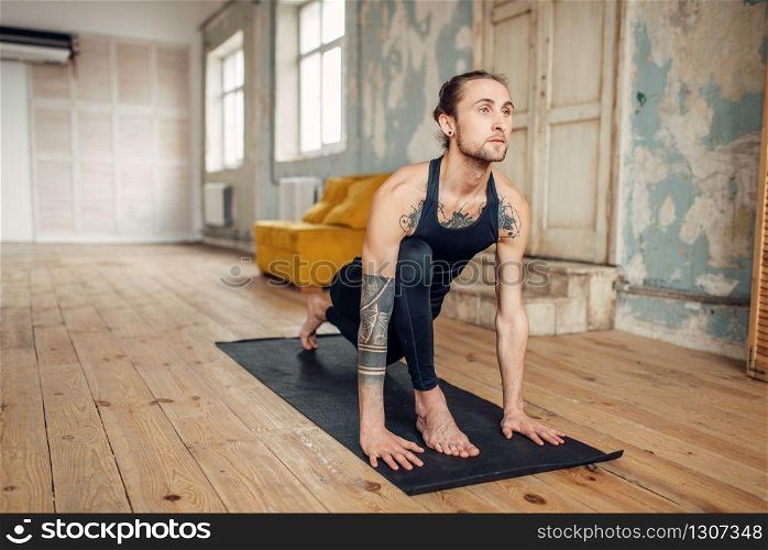 Male yoga with tattoo on hand doing exercise in gym with grunge interior. Fitness training indoors. Male yoga with tattoo on hand doing exercise