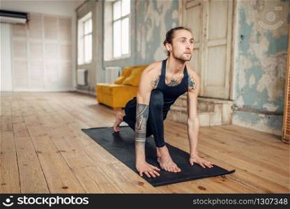 Male yoga with tattoo on hand doing exercise in gym with grunge interior. Fitness training indoors. Male yoga with tattoo on hand doing exercise