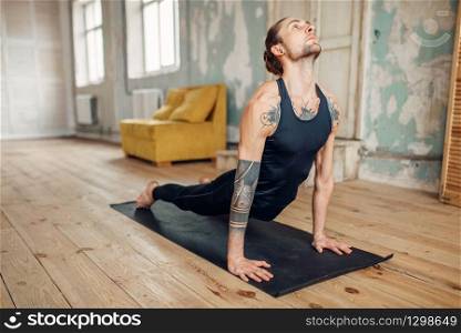 Male yoga with tattoo on hand doing push up exercise in gym with grunge interior. Fitness workout indoors. Male yoga doing push up exercise