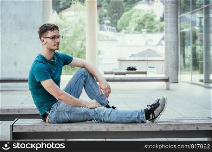 Male young employee is sitting outdoors, taking a break. Urban business setting.
