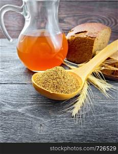Malt in a spoon, bread, kvass in a jug and spikelets on background of dark wooden board