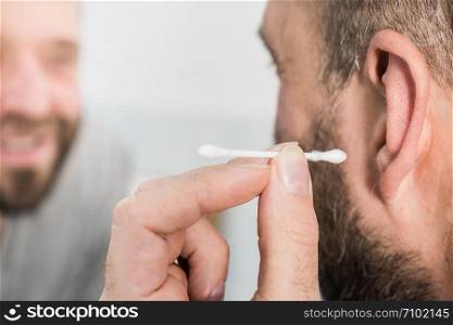 Man about to clean his ears using Q-tip cotton swab. Hygiene essentials concept. Removing wax from ear.. Man removing wax from ear using Q-tip