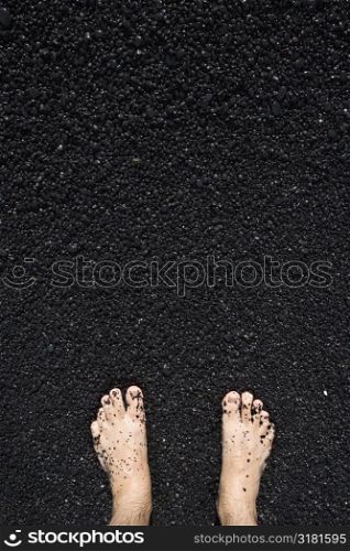 Man&acute;s barefeet in black sand in Maui, Hawaii.