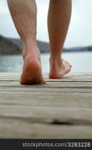 Man&acute;s feet walking on dock towards water.